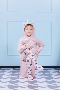 Tek boynuzlu at kostümlü güzel küçük bir kız gülümsüyor ve mavi duvarda eğleniyor. Mutlu çocukluk