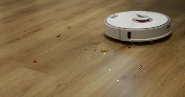 Fırçalı beyaz otomatik robot elektrikli süpürge Noel 'den sonra tahta zeminden konfeti temizliyor, doğum günü partisi. Belli bir zamanda dairenin otomatik temizlenmesi