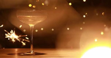 Bir bardak şampanya ve altın ışıklı karanlık bir arka plan ve yeni yıl maytapları.