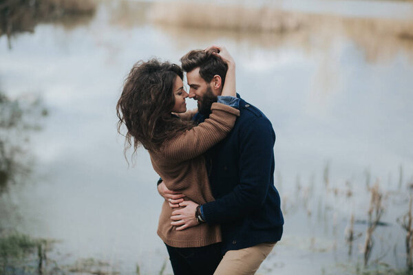 two caucasian lovers near the lake. Young couple is hugging on autumn day outdoors. A bearded man and curly woman in love. Valentine's Day. Concept of love and family.