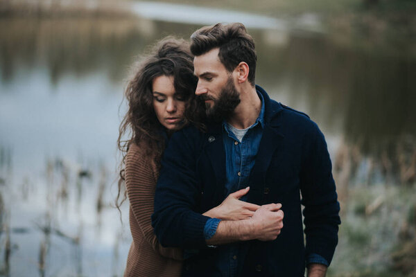 Два кавказских любовника у озера. Молодая пара обнимается осенним днем на открытом воздухе. Бородатый мужчина и кудрявая женщина влюблены. День Святого Валентина. Концепция любви и семьи.