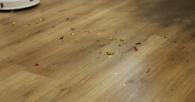 Fırçalı beyaz otomatik robot elektrikli süpürge Noel 'den sonra tahta zeminden konfeti temizliyor, doğum günü partisi. Belli bir zamanda dairenin otomatik temizlenmesi.