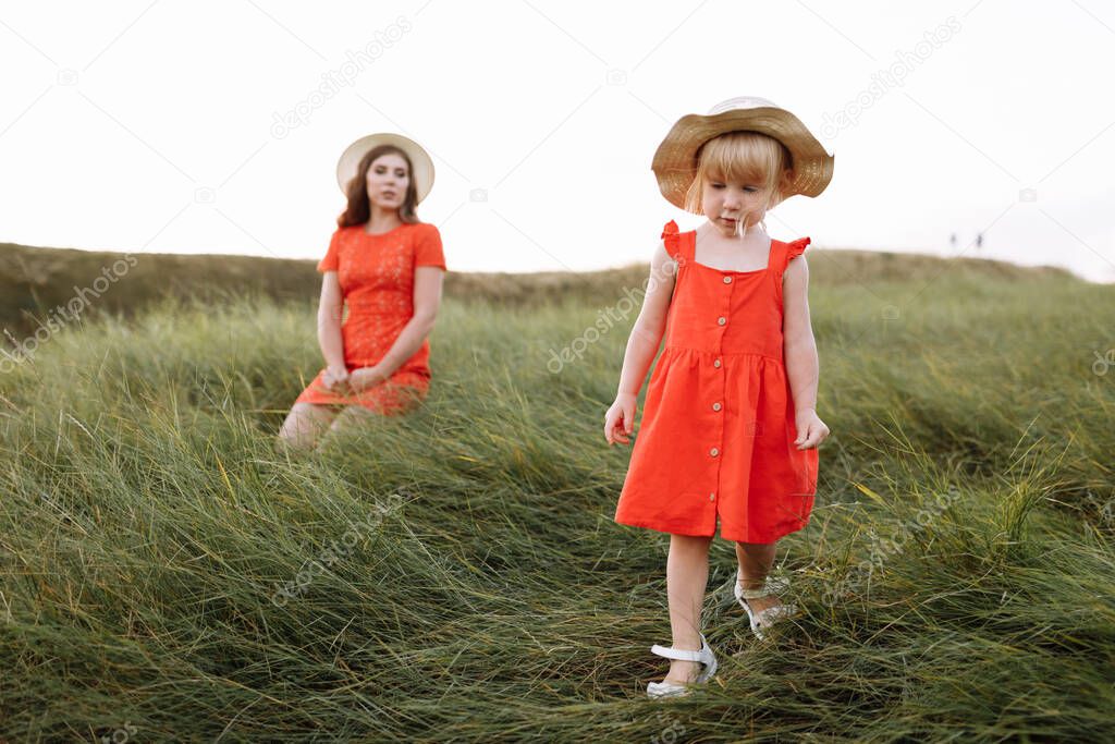 young beautiful mother and little daughter walking on nature on summer day vacation. Mom and girl playing in the field at the sunset time. mothers day. Concept of friendly family.