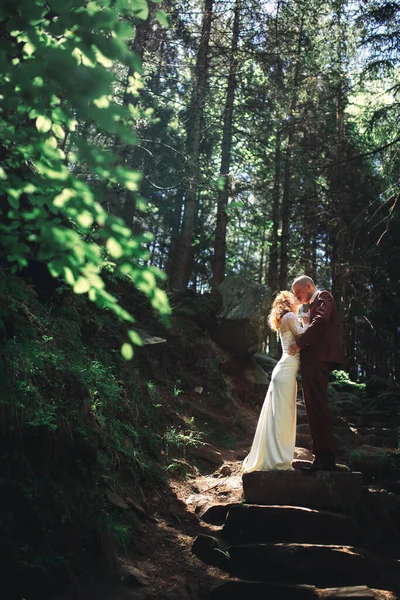 一对新婚夫妇在绿树成荫的森林里欢天喜地 穿着白色长裙的新娘和穿着红色西服的新郎拥抱在一起 婚礼当天 — 图库照片