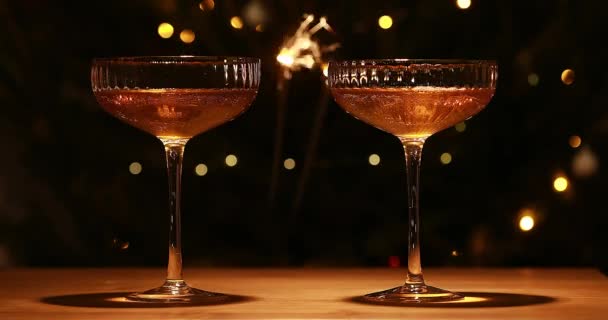 Dvě sklenice šampaňského a tmavé pozadí se slavnostními zlatými světly a novoroční jiskrou. — Stock video