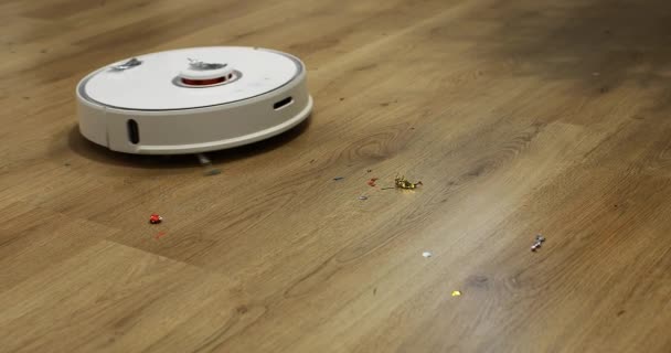 Aspiradora robot automática blanca con cepillos está limpiando confeti del piso de madera después de Navidad, fiesta de cumpleaños. limpieza automática del apartamento a una hora determinada. — Vídeo de stock