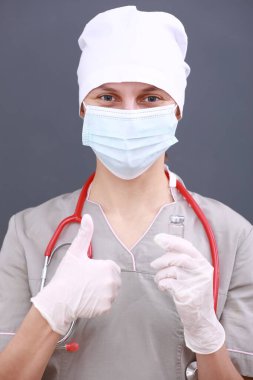 Doktor, tıbbi maske, steteskop ve eldiven giyen hemşire grip, kızamık, koronavirüs, Cvid-19 aşı hastalığı ve parmaklar yukarı. Tıbbi Konsept Corona Virüsü.