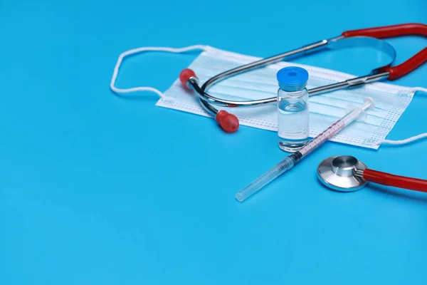 Medical bottle, vial, syringe, stethoscope and face mask on blue background with copy space. Vaccination session and immunity improvement