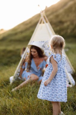 Güzel bir anne ve küçük kızı tarlada çadır başında oturuyor. Birlikte zaman geçirmek, dışarıda, tatilde, dışarıda. Bahçede ya da parkta güzel gün batımı ışığı