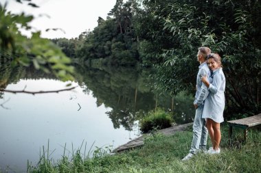 Genç çift güneşli bir günde göl kenarında sarılıp yürüyorlar. Yaz tatilindeki kadın ve erkek. Sevimli aile kavramı. seçici odak.