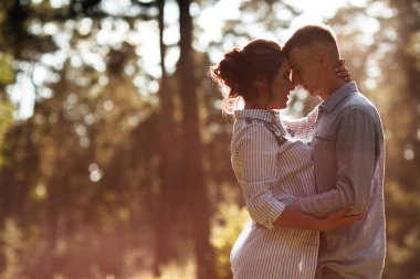 Neşeli genç kadın ve erkek yaz parkında kucaklaşıyorlar. Flört ve romantik tatil. Güneşli bir günde birbirine nazikçe bakan çift. Gençler arasındaki aşk ve ilişkiler.