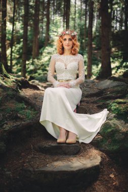 Ormanda, başında çiçekli bir çelenkle güzel, kızıl saçlı bir gelin. Yaz günü açık havada uzun beyaz elbiseli bir kadın. düğün günü.