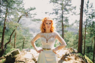 Ormanda, başında çiçekli bir çelenkle güzel, kızıl saçlı bir gelin. Yaz günü açık havada uzun beyaz elbiseli bir kadın. düğün günü.