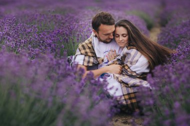 Genç çift yaz günü lavanta tarlasında oturup sarılıyorlar. Aşk hikayesi. Ekoseli kadın ve erkek açık havada..