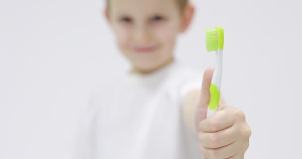 Ungar ler på nära håll. Porträtt leende pojke med tandborste. Pojke gör roligt ansikte medan borsta tänderna på vit bakgrund. Hälsovård, tandhygien. — Stockvideo