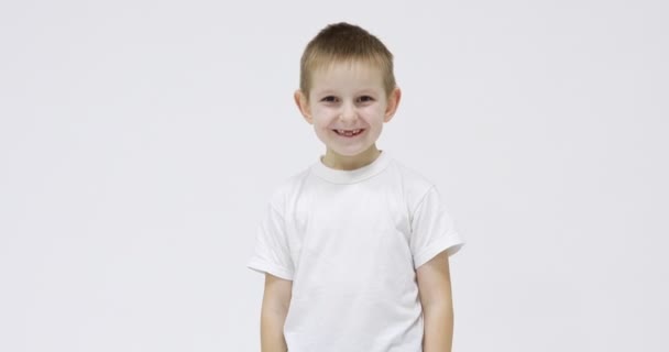 Beyaz tişörtlü mutlu çocuk beyaz arka planda bebek dişlerini nerede kaybettiğini göstermek için ağzını açıyor. — Stok video