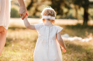 Yeni yürümeye başlayan çocuğa bak. Annenin el ele tutuşup doğanın tadını çıkardığını ve yaz parkında yürüdüğünü görmek. Genç bir aile tatilde, dışarıda birlikte vakit geçiriyor. Anneler günü, bebekler günü.