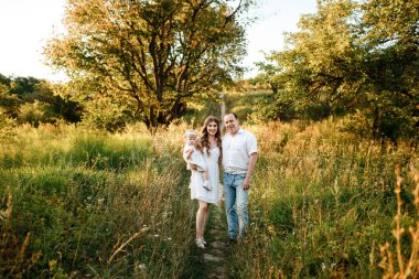 Aile, ebeveynlik, eğlence ve insan konsepti - mutlu anne, baba ve küçük kız yaz parkında oynuyorlar. Genç bir aile tatilde, dışarıda birlikte vakit geçiriyor.