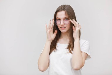 Beyaz arka planda kameraya dik dik bakan, somurtkan ofis kızı. Göz giysisini ayarlayan genç bir kadın. Gözlüklü konsept.