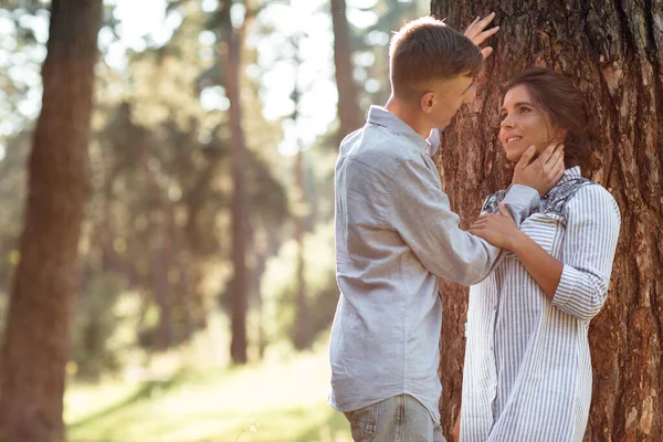 年轻夫妇在夏日公园的树旁拥抱 穿着斜纹棉布衣服的漂亮女人和男人都在外面玩得很开心 也在约会 浪漫的关系 情人节当天 — 图库照片