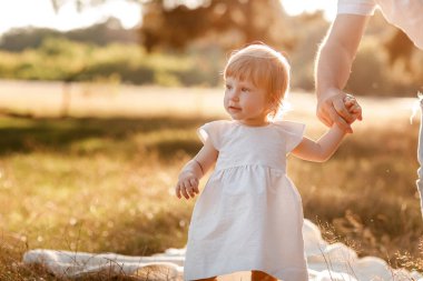 Yeni yürümeye başlayan çocuğa bak. Baba el ele tutuşur kız doğanın tadını çıkarır ve parkta yürür. Genç bir aile tatilde, dışarıda birlikte vakit geçiriyor. Babalar günü, bebekler günü. Aile yaz tatili kavramı