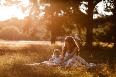 Genç ve güzel anne güneşli parkta küçük kızıyla yürüyor. Açık havada yaz tatili kavramı. Anneler günü, bebekler günü. Birlikte vakit geçirmek. Güneş ışığı