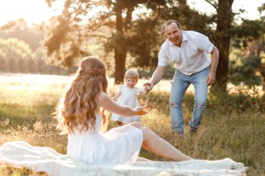 Anne, baba ve kızı parkta sarılıyor, eğleniyor ve yürüyorlar. Genç bir aile tatilde, dışarıda birlikte vakit geçiriyor. Yaz tatili kavramı.