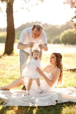 Anne, baba ve kızı parkta sarılıyor, eğleniyor ve yürüyorlar. Genç bir aile tatilde, dışarıda birlikte vakit geçiriyor. Yaz tatili kavramı