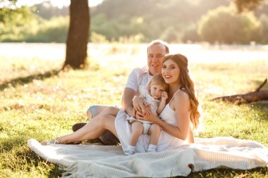 Anne, baba ve kızı parkta sarılıyor, eğleniyor ve yürüyorlar. Genç bir aile tatilde, dışarıda birlikte vakit geçiriyor. Yaz tatili kavramı