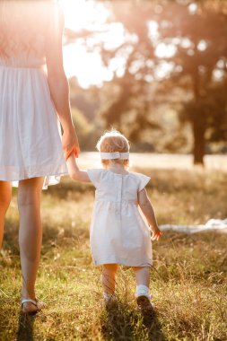 Yeni yürümeye başlayan çocuğa bak. Annenin el ele tutuşup doğanın tadını çıkardığını ve yaz parkında yürüdüğünü görmek. Genç bir aile tatilde, dışarıda birlikte vakit geçiriyor. Anneler günü, bebekler günü.