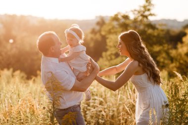 Aile, ebeveynlik, eğlence ve insan konsepti - mutlu anne, baba ve küçük kız yaz parkında oynuyorlar. Genç bir aile tatilde, dışarıda birlikte vakit geçiriyor.
