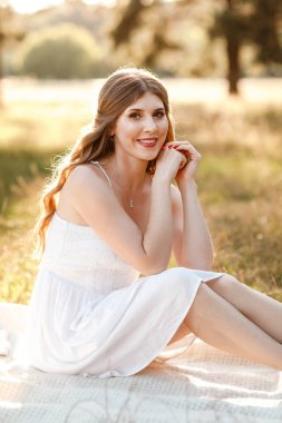 Genç, sarışın, uzun saçlı, beyaz elbiseli bir kadın. Hafta sonunu şehir dışında, açık havada, çayırdaki parkta piknik yaparak geçirir..