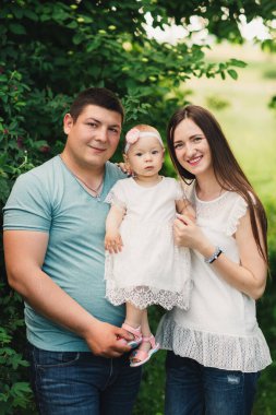 Aile yaz parkında hayattan zevk alıyor. Dışarıda mutlu, genç bir aile. Anne, baba dışarıda kızlarına sarılıyor ve doğada eğleniyorlar. Aile yaz tatili kavramı.