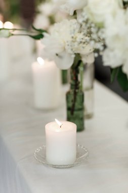 Düğün resepsiyonunda masa hazır. Modern olay tasarımı. Çiçekleri ve yeşilliği olan çiçek kompozisyonları, dekore edilmiş masalarda mumlar. Çiçekler ve mum ışığı olan masa ayarları