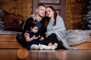 Anne, baba ve kız Noel ve yeni yılı kutluyorlar. Ebeveynler ve küçük çocuklar içeride Noel ağacı yakınında eğleniyorlar. Noel 'den önceki sabah. Portre yakın çekim.