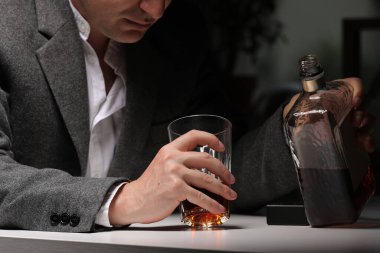 Adam işten sonra mutfakta bir bardağa alkol dolduruyor. Şiddetli baş ağrısı ya da migrenden muzdarip genç bir adam mutfakta bir bardak viskiyle oturuyor. alkol bağımlılığı.