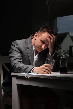 Adam işten sonra mutfakta alkol içiyor. Genç adam şiddetli baş ağrısı ya da migrenden muzdarip mutfakta bir bardak viskiyle oturuyor. alkol bağımlılığı.