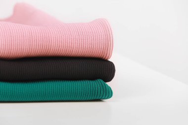 Beyaz arka planda katlanmış farklı örgü desenleri olan örülmüş sıcak renkli süveter yığını, beyaz duvar arka planı. Sonbahar mevsimi örgü. Kapat, metin için boşluk kopyala.