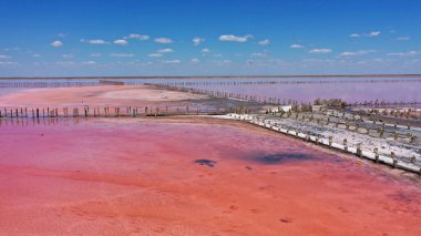 Genichesk, Ukrayna 'daki pembe bir gölde tuz toplamak için ahşap yapıların hava aracı görüntüsü. Göl, tuzlar ve sudaki kabuklu deniz ürünleri yüzünden doğal olarak pembeleşir.