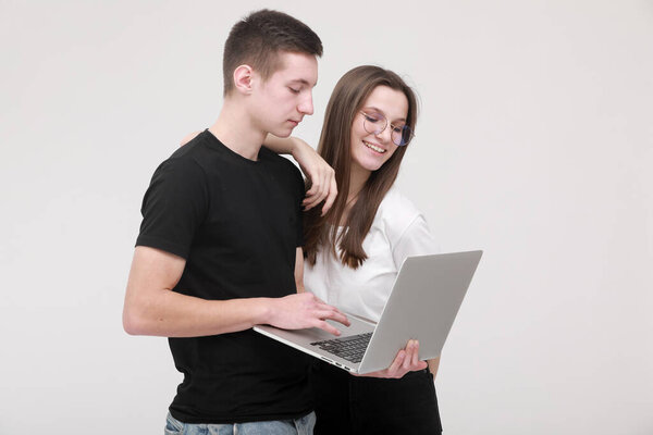 Portrait of a smiling teens boy and girl holding laptop computer while standing and looking in it isolated over white wall background. Study and work