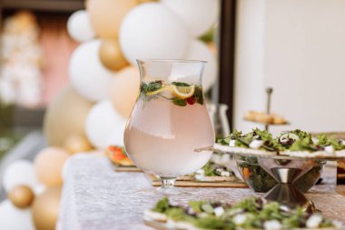 Limonata dolu büyük cam sürahiler bir ışık masasında duruyor. Meyve, portakal, limon, greyfurt, ahududu ve nane dilimlerinde. Kutlama partisi