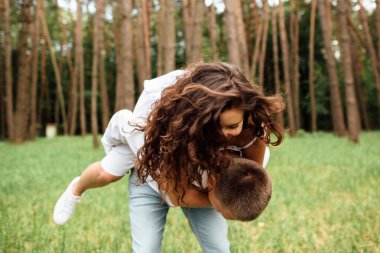 Gülen çift parkta eğleniyor. Aşk ve şefkat, flört, romantizm, aşıklar yaz parkında birbirlerinden hoşlanırlar. Erkek sırtında güzel kıvırcık saçlı kadın gülümsüyor ve gülüyor.