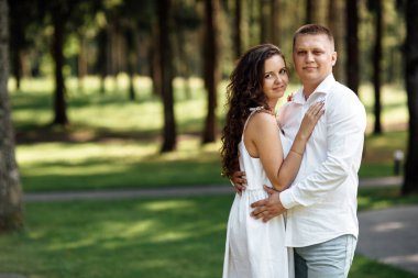 Genç aşık çift bir yaz günü parkta sarılıyor. Erkek ve kadın açık havada.