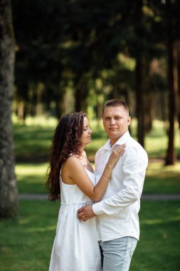 Genç aşık çift bir yaz günü parkta sarılıyor. Erkek ve kadın açık havada.