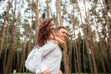 Gülen çift parkta eğleniyor. Aşk ve şefkat, flört, romantizm, aşıklar yaz parkında birbirlerinden hoşlanırlar. Erkek sırtında güzel kıvırcık saçlı kadın gülümsüyor ve gülüyor.