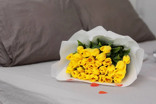 bouquet of yellow tulips with red hearts confetti in bed in bedroom. Concept of holiday, birthday, Women Day. surprise in bed. Good morning. still life. holiday gift concept. Romantic background.