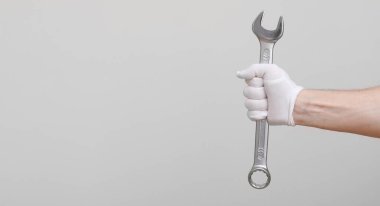 Bir işçi, inşaatçı, tamirci, tamirci, beyaz arka planda İngiliz anahtarı tutan koruma eldivenli eller..