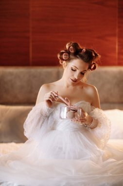 Güzel, gülümseyen bir esmer kadının güzel portresi. Parlak makyajlı, nefis Fransız kurabiyeleri ya da kurabiyeler yiyen bir kadın. Beyaz elbiseli ve pembe bukleli kız yatakta oturuyor ve rahatlıyor..