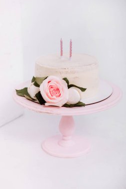 Beyaz stüdyoda 2 yıllık mum ve güllerle süslenmiş güzel beyaz kremalı pasta. Doğum günü partisi - Doğum yılı kavramı, parti, yaşam kutlaması ve unutulmaz anlar