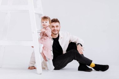 Şık bir adam süslemeli stüdyoda güzel bir kız bebekle eğleniyor. Kızı merdivene tırmanmaya çalışıyor. Çocukluk aile kavramını seviyorum. Babalar günü, sevgi, derin bağlılık ilişkileri..